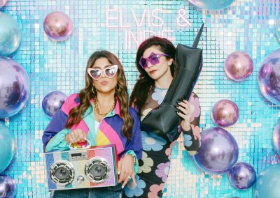 Two guests with retro props posing on a sequin backdrop at a bat mitzvah photo booth