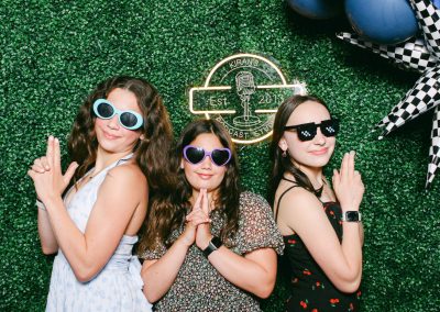 Teens in sunglasses posing at a greenery wall with a custom neon sign at a Minneapolis mitzvah photo booth