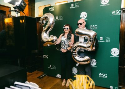 Two guests with props and balloons in front of a branded step and repeat backdrop at a corporate anniversary party photo booth in Minneapolis