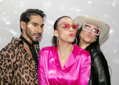 Three guests in colorful outfits and props posing in an open style photo booth for a shareable Instagram photo