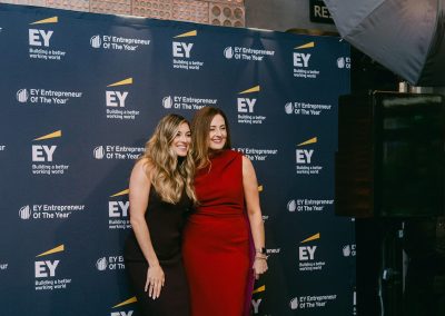 Two guests posing at a branded step and repeat photo booth backdrop creating social media content