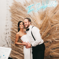 Couple posing at a pampas grass backdrop with a custom neon name sign
