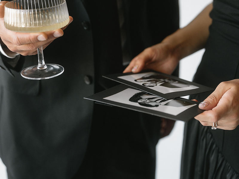 Guest holding a cocktail and black and white open style photo booth prints
