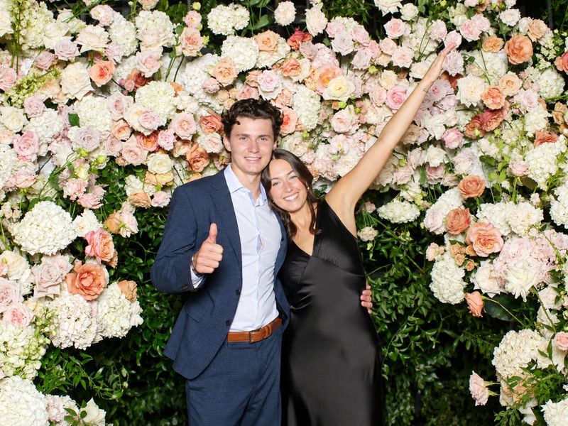 Couple posing in front of a flower wall backdrop at an open style photo booth