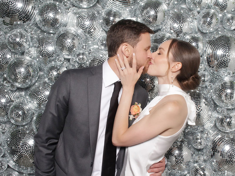 Couple kissing in front of a disco ball wall backdrop at an open style photo booth