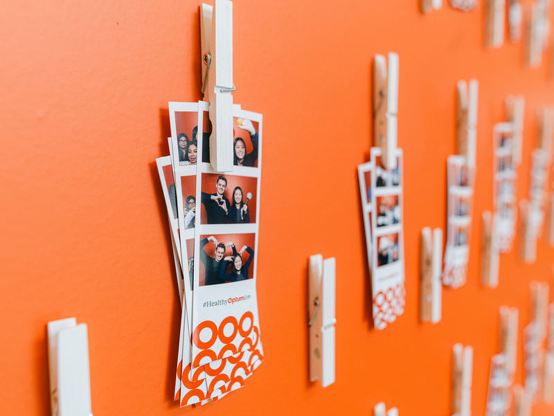 Photo strips clipped to an orange wall display at an open style photo booth