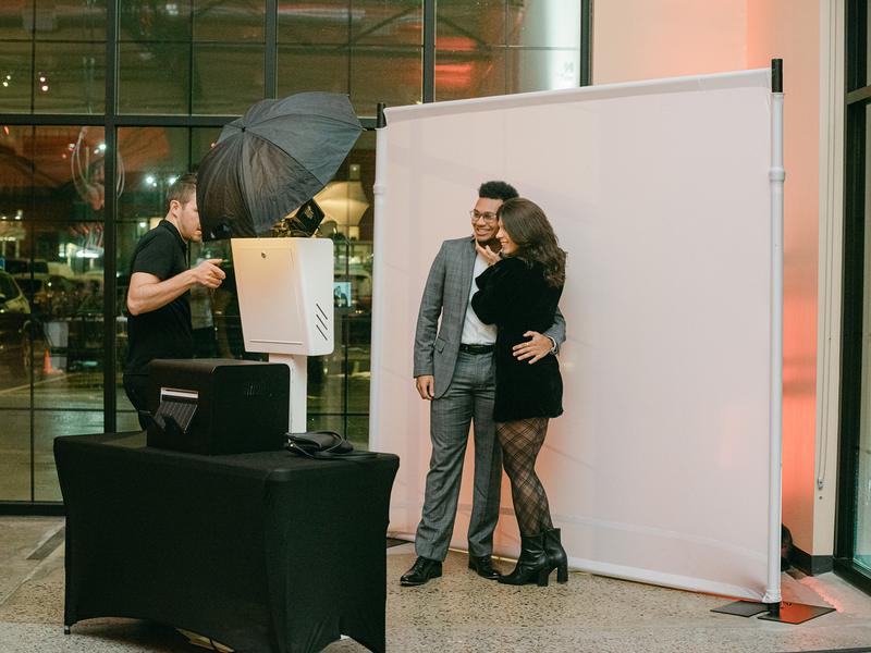 Open style photo booth with white backdrop and attendant at an event