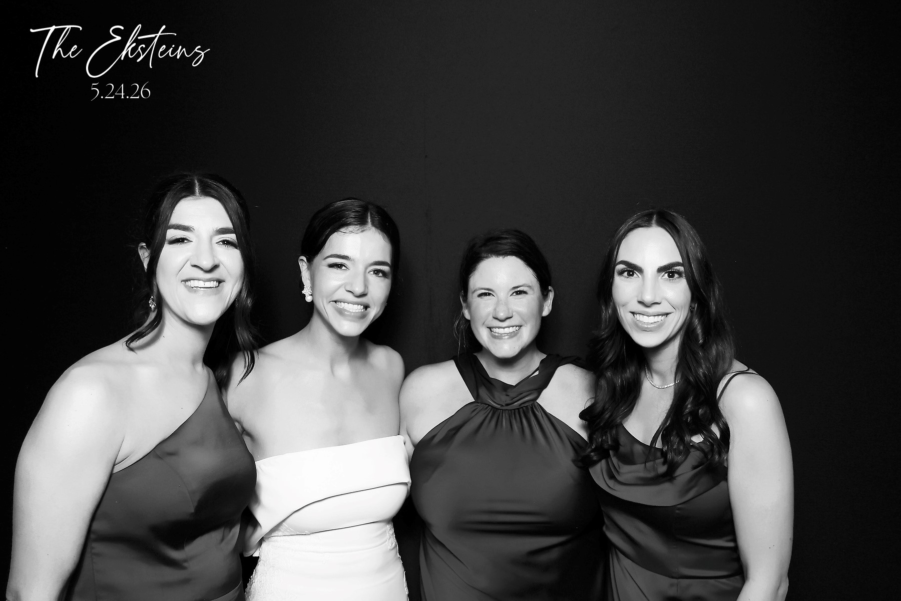 Reverse glam black and white photo booth portrait of a bride and three friends lit against a black backdrop