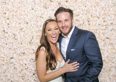 Bride and groom laughing in an open style photo booth in front of a blush flower wall backdrop