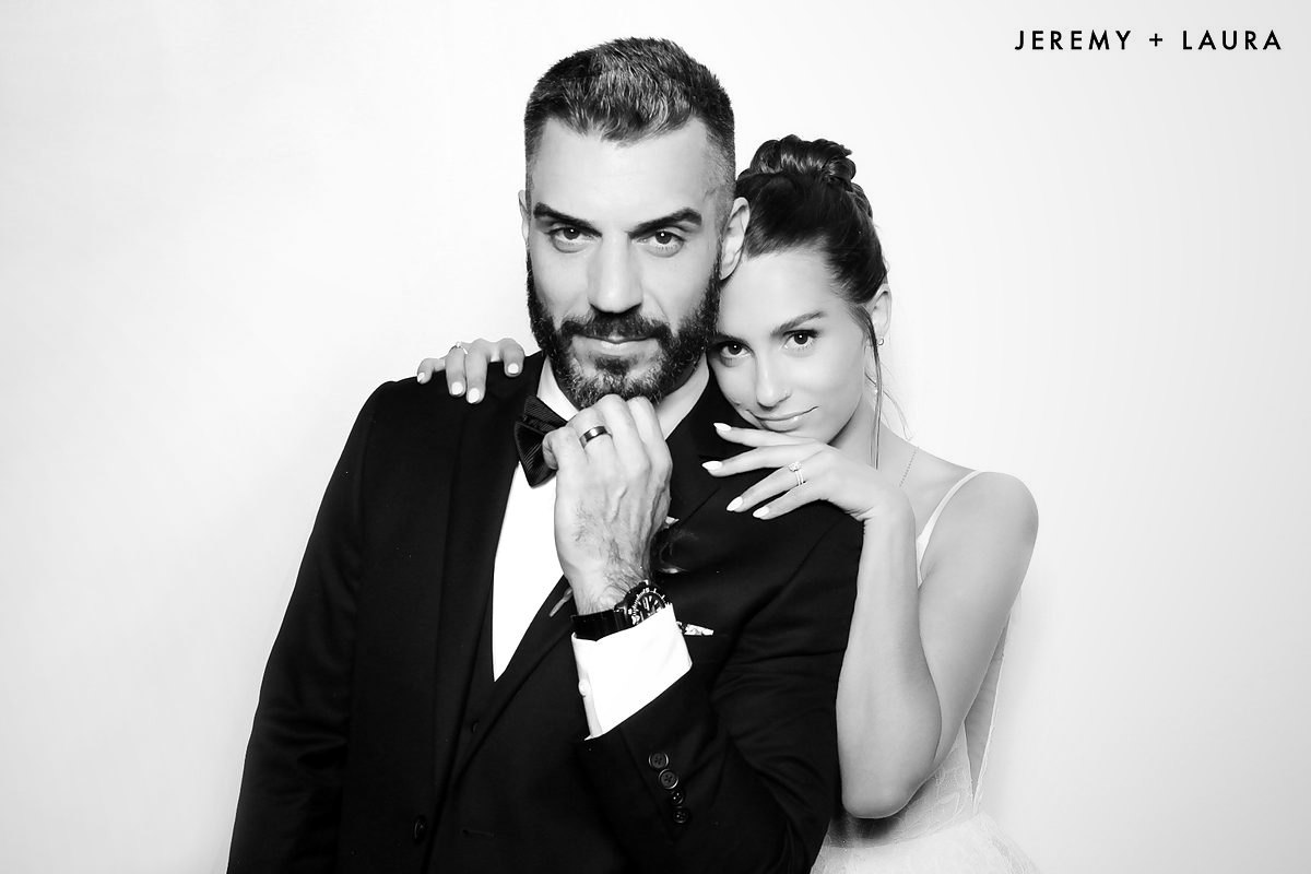 Couple in a tuxedo and white dress posing in a black and white glam photo booth
