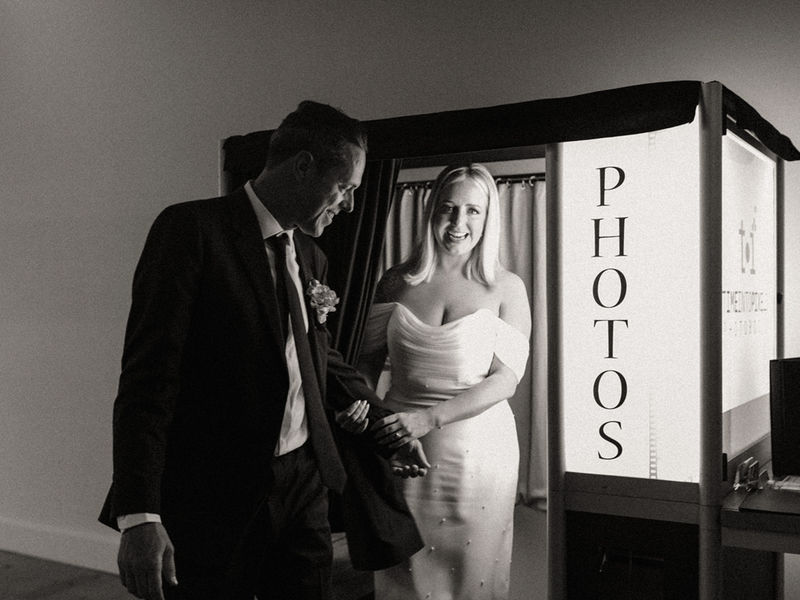 Black and white photo of a wedding couple stepping out of a traditional photo booth
