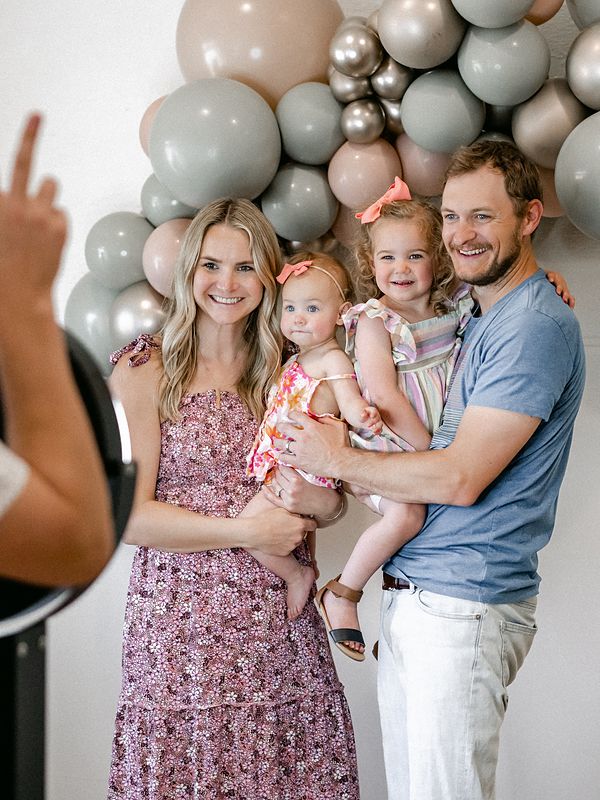 Family with two little girls posing at a boomerang booth in front of a balloon garland