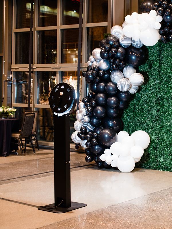 Boomerang booth kiosk next to a greenery wall with black and white balloons at a corporate event