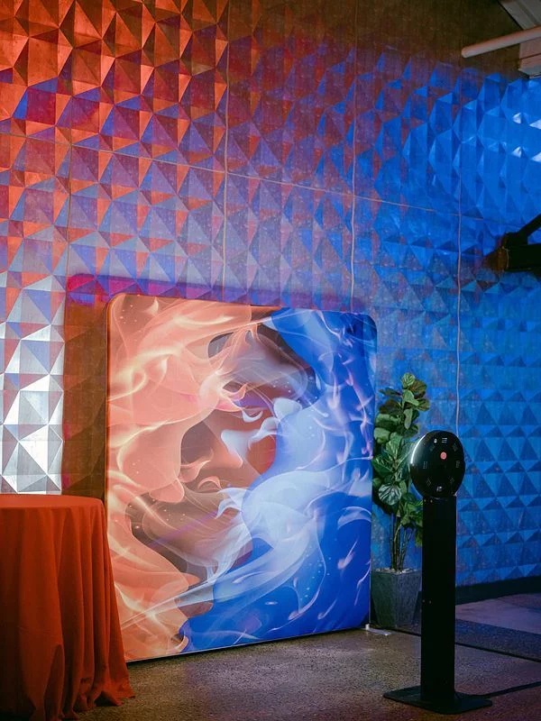 Boomerang booth kiosk beside a printed backdrop lit in red and blue at an evening event