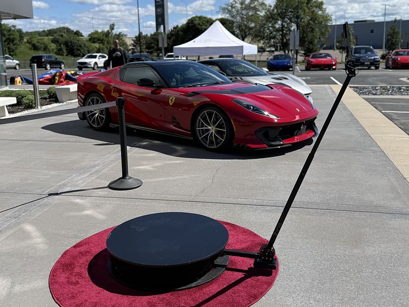360 photo booth platform on a red carpet ring next to a sports car at a dealership event