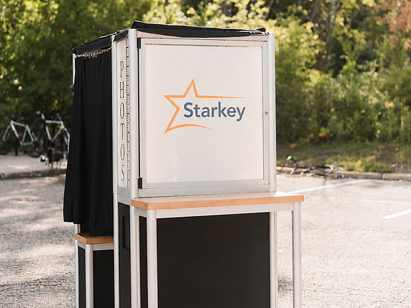 Branded enclosed photo booth with a company logo panel at an outdoor corporate event