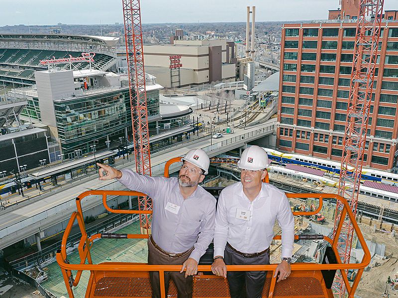 Two guests in hard hats on a lift above a city construction site, branded green screen photo