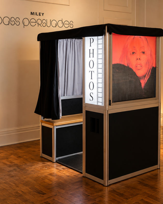 Enclosed photo booth with curtain and lit PHOTOS panel at a brand launch event