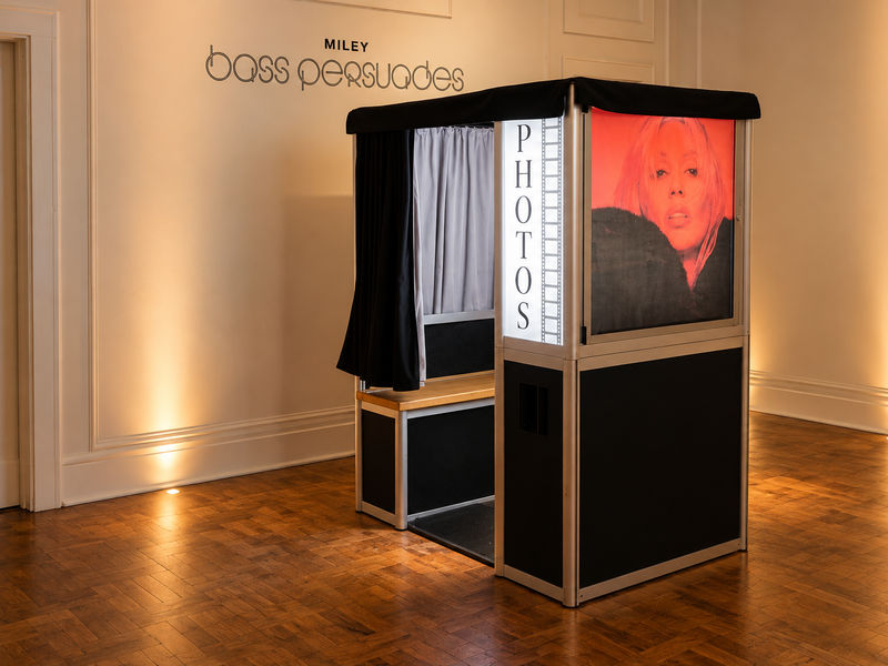 Enclosed photo booth with curtain and lit PHOTOS panel at a brand launch event