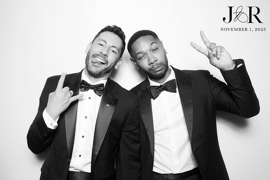 Two guests in tuxedos posing in a black and white glam booth portrait