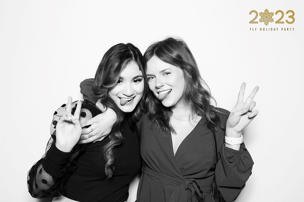 Two friends making peace signs in a black and white glam booth photo at a 2023 holiday party