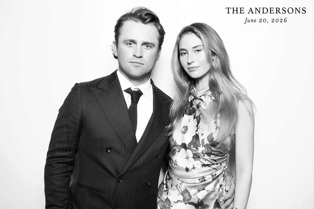 Couple in a pinstripe suit and floral dress posing in a black and white glam booth at a 2026 wedding