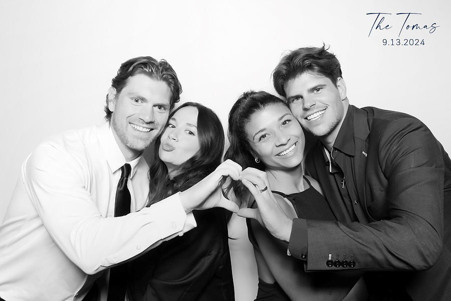 Two couples making heart hands in a black and white glam photo booth portrait