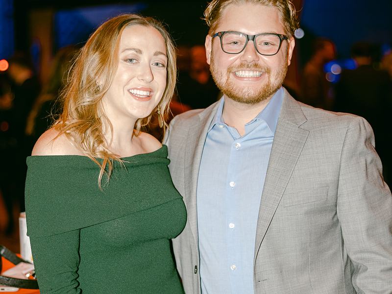 Couple in a green dress and gray suit posing at a corporate party