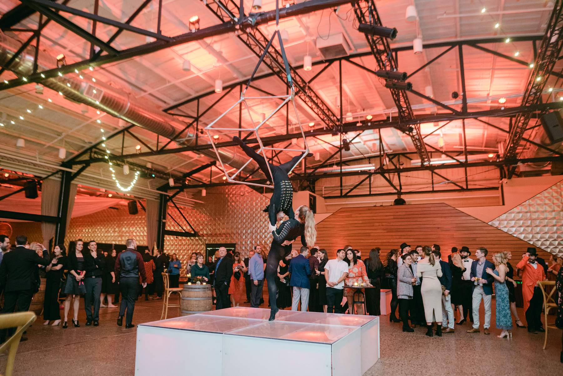 Aerialist duo performing on a hanging frame above guests at a warehouse company party
