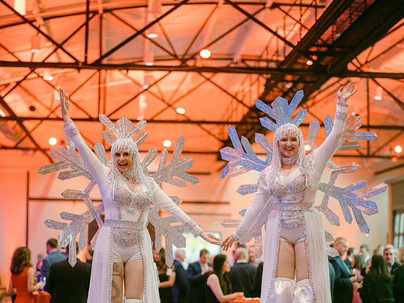 Stilt walkers in white costumes among guests at a warehouse party