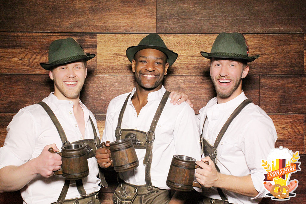 Oktoberfest company party print of three men in lederhosen and alpine hats toasting with beer steins