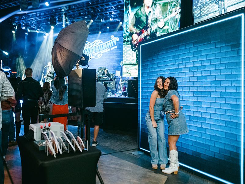 Guests posing at a lit brick wall backdrop at a sales summit photo booth activation