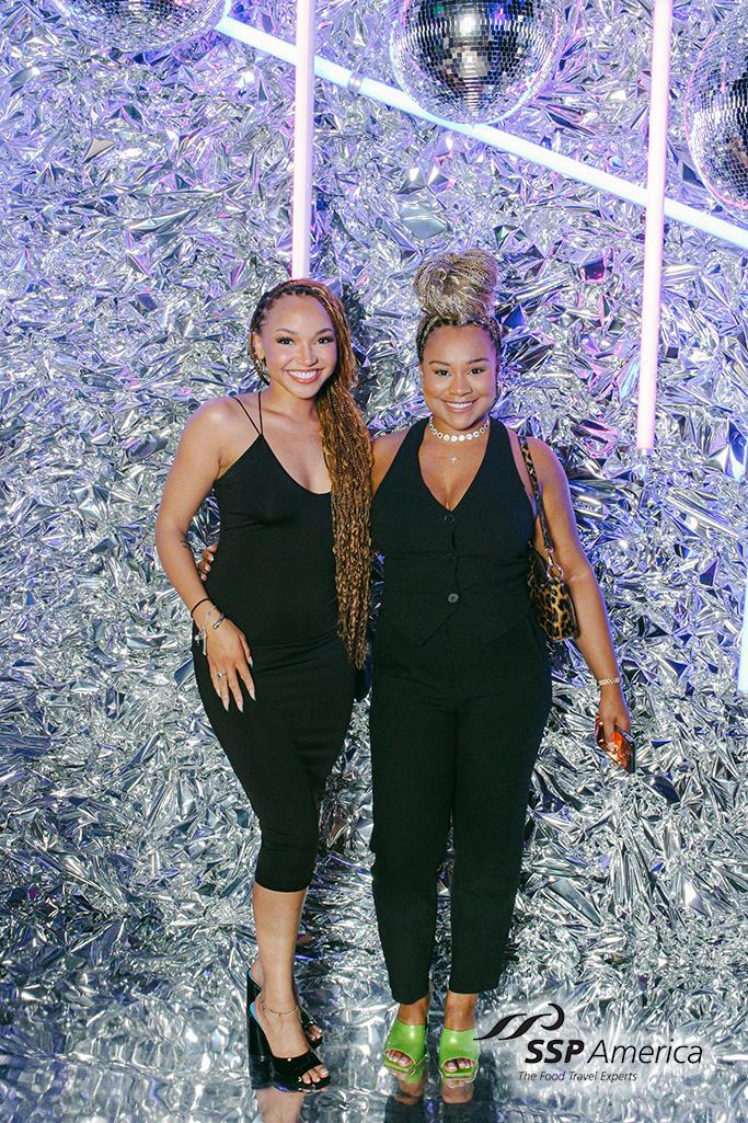 Two women posing on a silver tinsel backdrop with a disco ball at a corporate party, portrait print