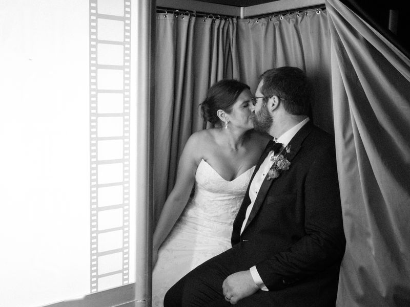 Wedding couple kissing inside an enclosed photo booth behind the curtain