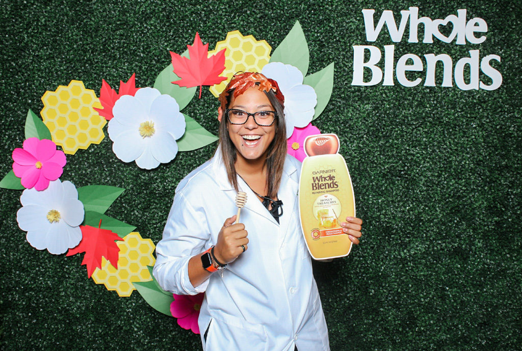 Whole Blends brand activation print of a woman in a lab coat holding a giant shampoo bottle prop